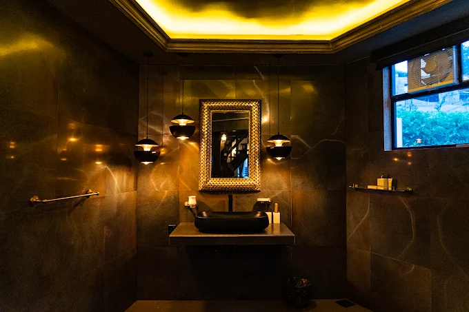 Dark stone bathroom with brass pendant lights and a gold framed mirror